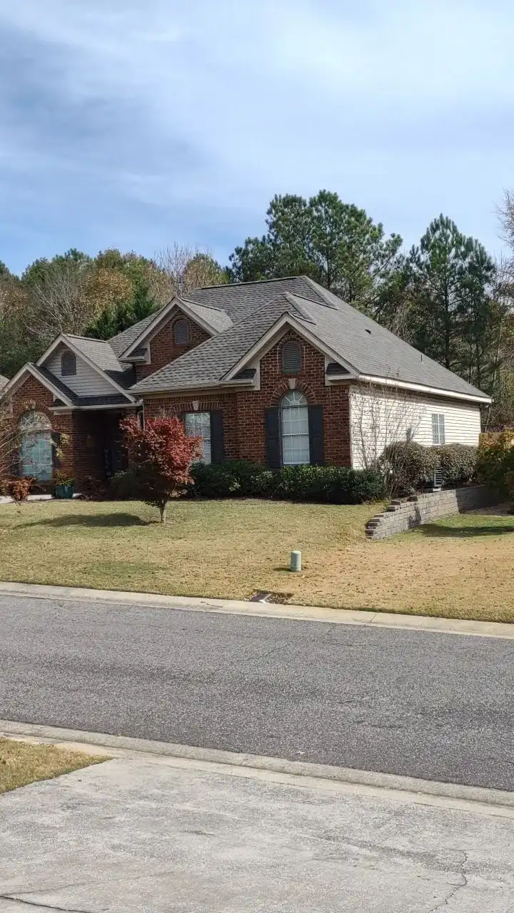 A large brick house with a shingled roof, surrounded by trees and bushes.